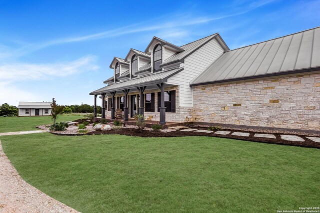 view of side of property featuring a porch, a standing seam roof, metal roof, a yard, and stone siding