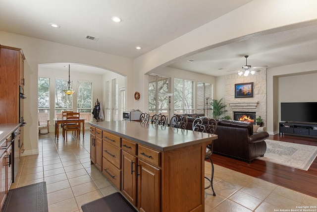 kitchen with arched walkways, a ceiling fan, brown cabinetry, a breakfast bar, and light tile patterned floors