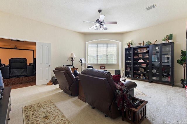 living room featuring a textured ceiling, carpet floors, visible vents, and a ceiling fan