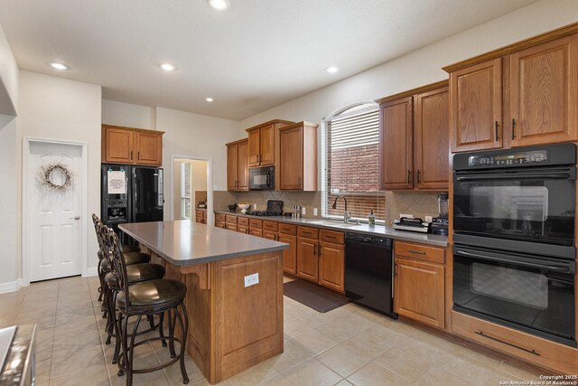 kitchen with a sink, backsplash, a breakfast bar, a kitchen island, and black appliances