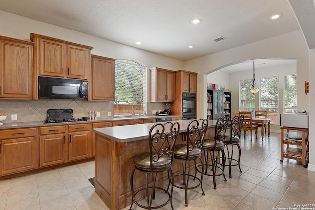 kitchen with decorative backsplash, arched walkways, a kitchen bar, and black appliances