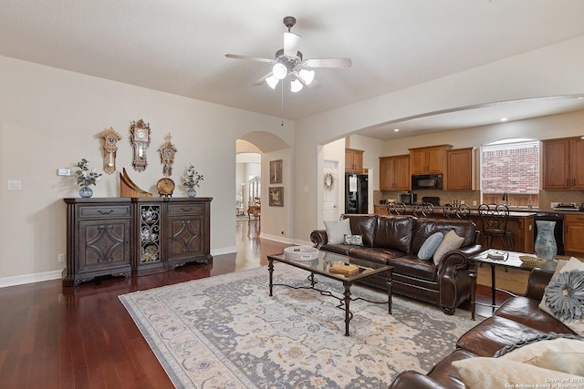 living room featuring arched walkways, dark wood finished floors, baseboards, and ceiling fan