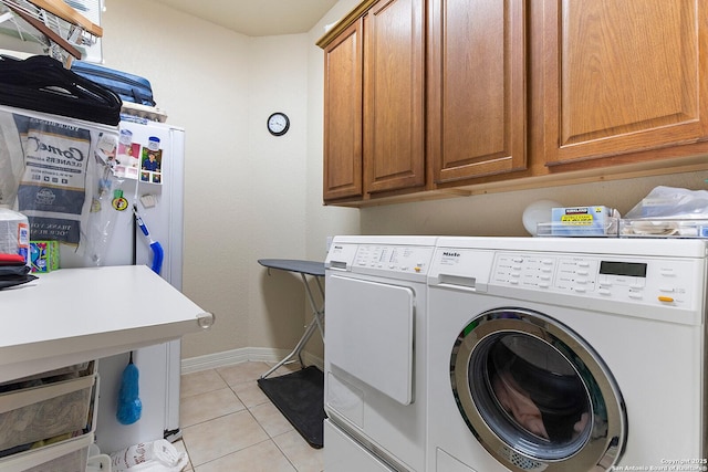 clothes washing area with cabinet space, washing machine and dryer, baseboards, and light tile patterned floors
