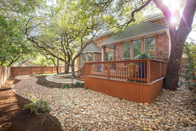 rear view of property featuring a fenced backyard, a wooden deck, brick siding, and a shingled roof