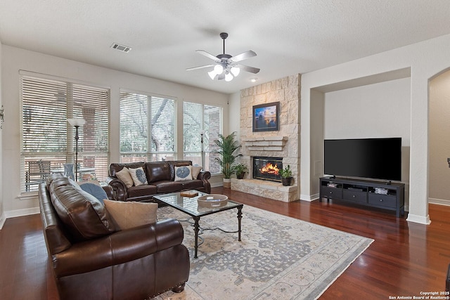 living area with a ceiling fan, wood finished floors, a stone fireplace, baseboards, and visible vents