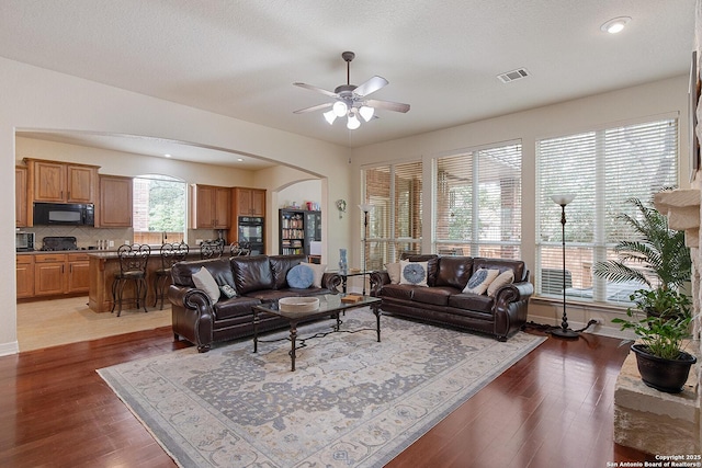 living area with wood finished floors, visible vents, arched walkways, and ceiling fan