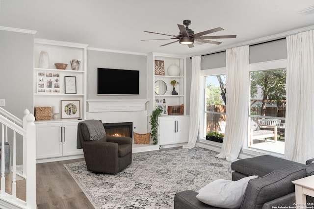21707 Beaver Bnd, San Antonio, TX 78258 - living area featuring wood finished floors, a ceiling fan, crown molding, a tiled fireplace, and built in shelves