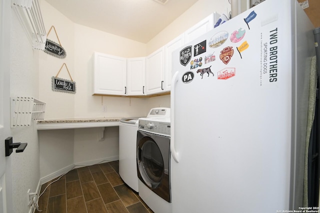 clothes washing area featuring washing machine and dryer, dark wood-type flooring, baseboards, and cabinet space