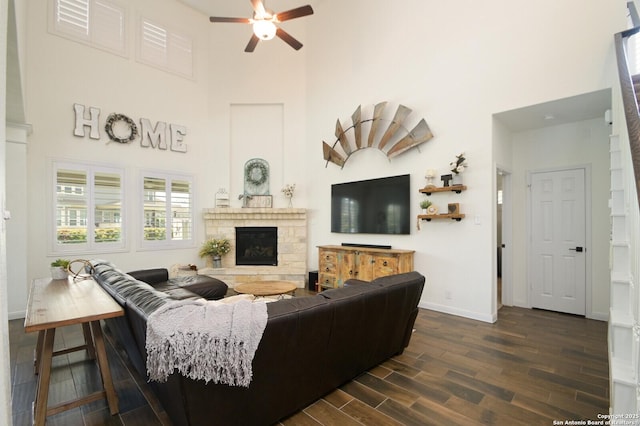 living area with a high ceiling, dark wood-style floors, a ceiling fan, baseboards, and a fireplace