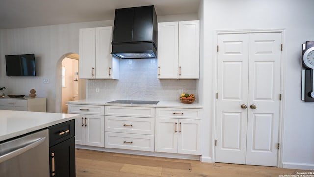 kitchen featuring white cabinets, light countertops, arched walkways, wall chimney range hood, and dishwasher
