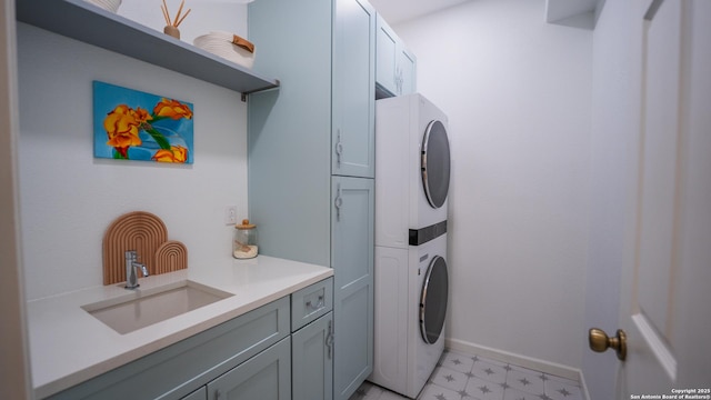 laundry area featuring a sink, light floors, cabinet space, baseboards, and stacked washer and clothes dryer