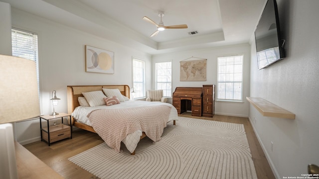 bedroom with a tray ceiling, wood finished floors, visible vents, a ceiling fan, and baseboards