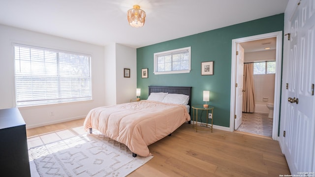 bedroom featuring ensuite bathroom, baseboards, and light wood-style floors