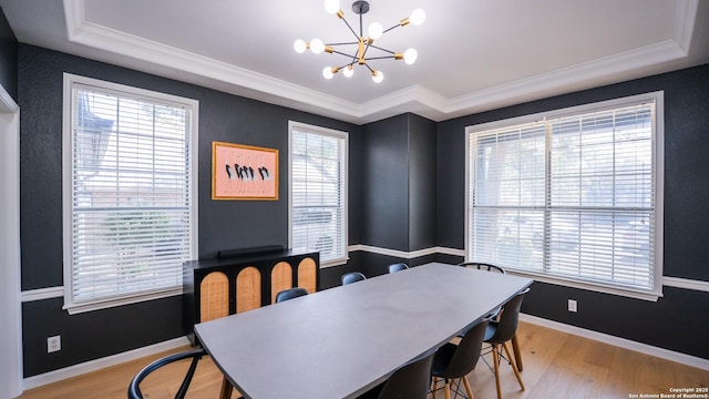 dining room featuring crown molding, light wood-style flooring, a chandelier, a raised ceiling, and baseboards