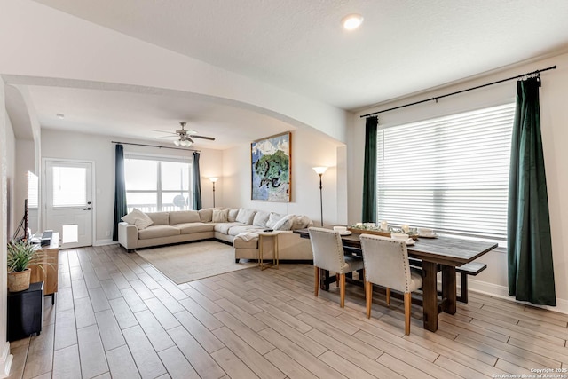 dining space featuring arched walkways, light wood finished floors, baseboards, and a ceiling fan