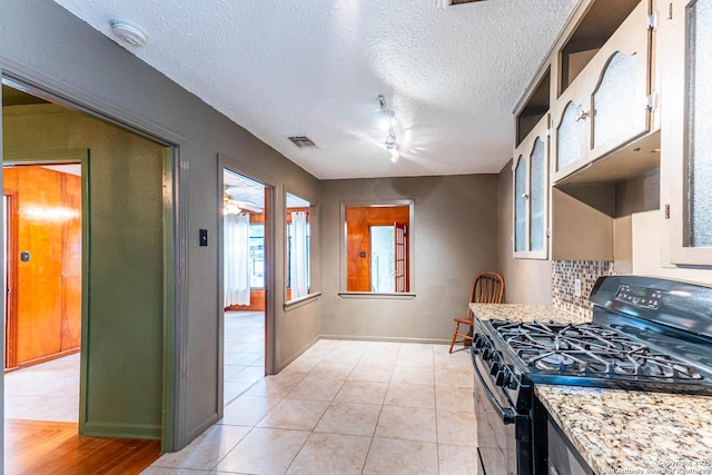 kitchen with black range with gas stovetop, decorative backsplash, light tile patterned flooring, glass insert cabinets, and visible vents