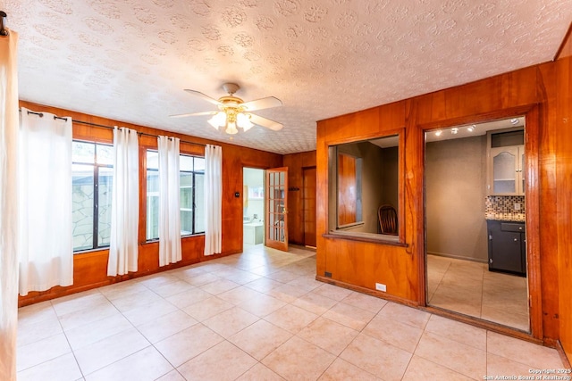 empty room with a textured ceiling, baseboards, a ceiling fan, wood walls, and light tile patterned floors