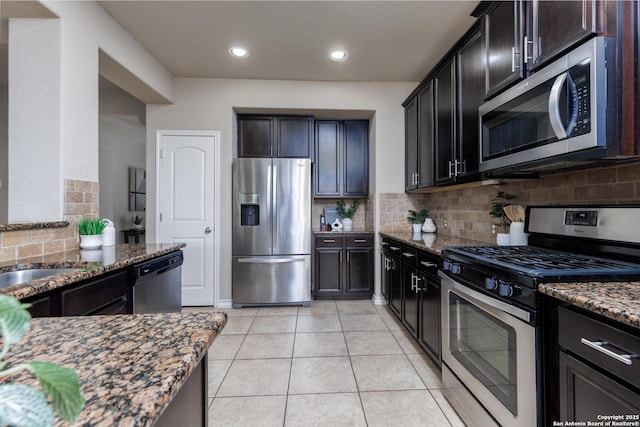 kitchen with tasteful backsplash, dark stone countertops, a sink, light tile patterned floors, and appliances with stainless steel finishes