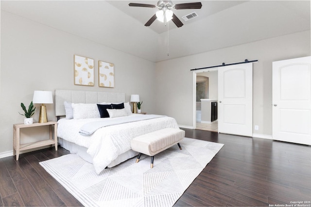 bedroom featuring a barn door, vaulted ceiling, wood finished floors, baseboards, and visible vents