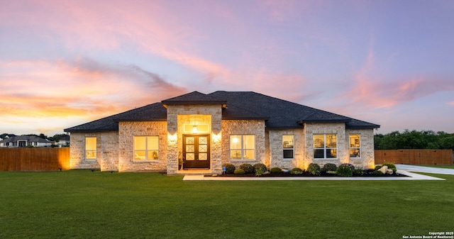 prairie-style house with fence, a lawn, a shingled roof, and stone siding