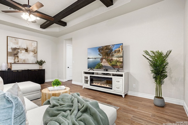 living area with baseboards, coffered ceiling, beamed ceiling, a ceiling fan, and wood finished floors