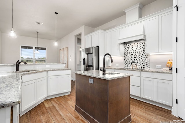 kitchen featuring light wood finished floors, a center island with sink, a sink, and stainless steel fridge with ice dispenser