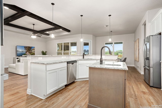 kitchen featuring open floor plan, light wood-style floors, stainless steel appliances, a center island with sink, and white cabinets