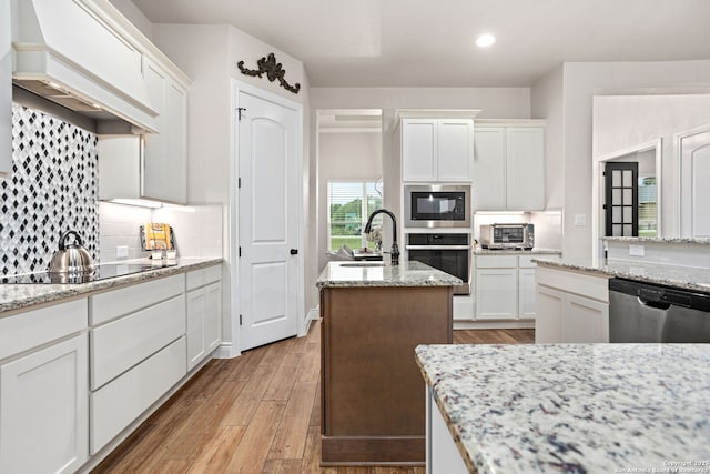 kitchen featuring custom exhaust hood, tasteful backsplash, a sink, light wood-type flooring, and stainless steel appliances