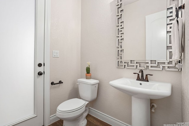 half bath featuring a sink, toilet, wood finished floors, and baseboards