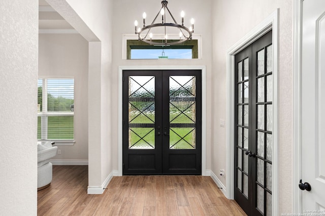 foyer entrance featuring a chandelier, wood finished floors, baseboards, and french doors
