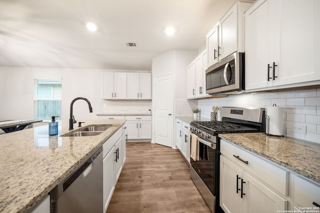 kitchen with a sink, light wood-style flooring, backsplash, appliances with stainless steel finishes, and visible vents