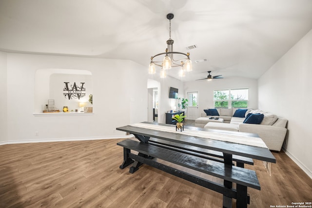 dining room featuring ceiling fan with notable chandelier, wood finished floors, visible vents, and vaulted ceiling