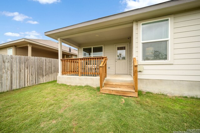 view of exterior entry with fence and a lawn
