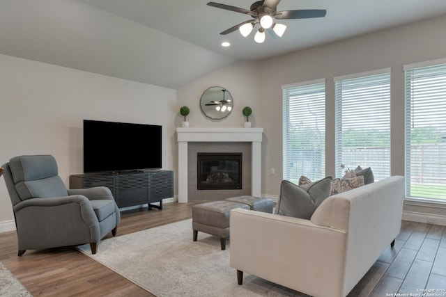 living room with a ceiling fan, wood finished floors, a tiled fireplace, baseboards, and lofted ceiling