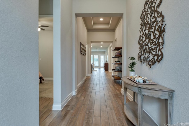 hallway featuring a textured wall, wood finished floors, recessed lighting, and a tray ceiling