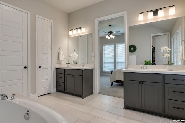 ensuite bathroom featuring ceiling fan, two vanities, a tub, and a sink
