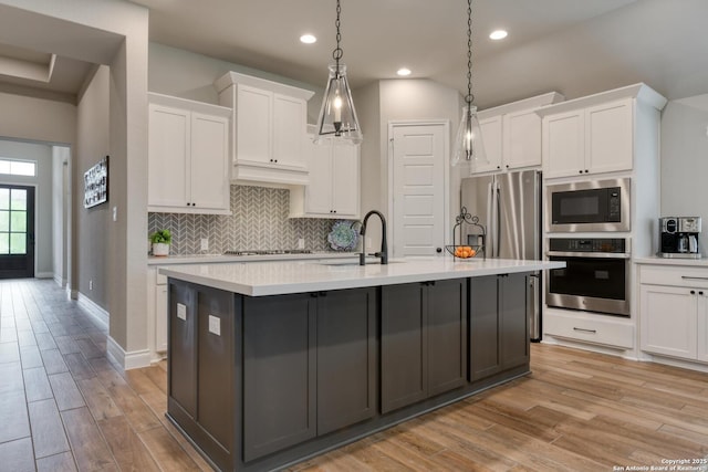 kitchen with white cabinets, a sink, backsplash, light countertops, and appliances with stainless steel finishes