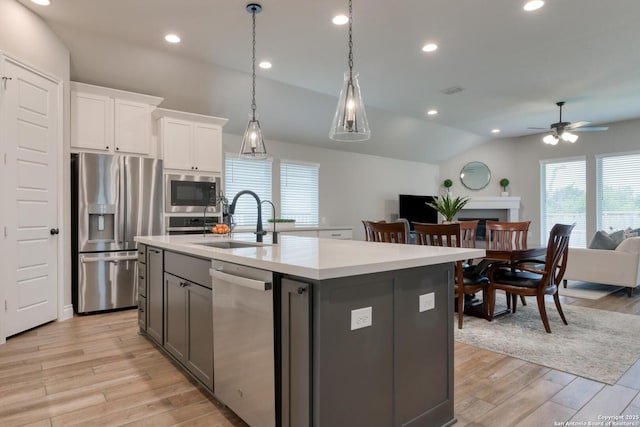 kitchen with a sink, open floor plan, vaulted ceiling, ceiling fan, and appliances with stainless steel finishes