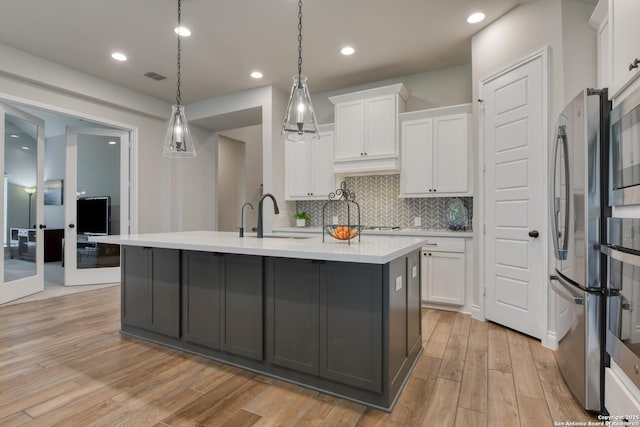 kitchen with white cabinets, light countertops, freestanding refrigerator, and light wood-style flooring