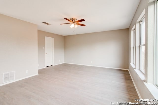 empty room featuring a ceiling fan, visible vents, wood finished floors, and baseboards