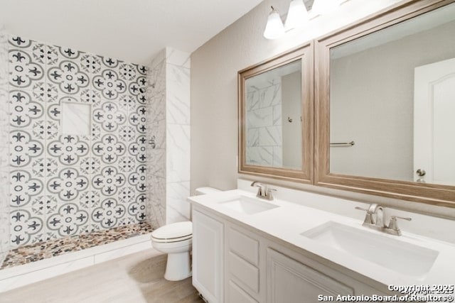 bathroom with double vanity, toilet, tiled shower, and a sink