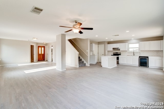 unfurnished living room featuring a sink, wine cooler, visible vents, and light wood-style floors