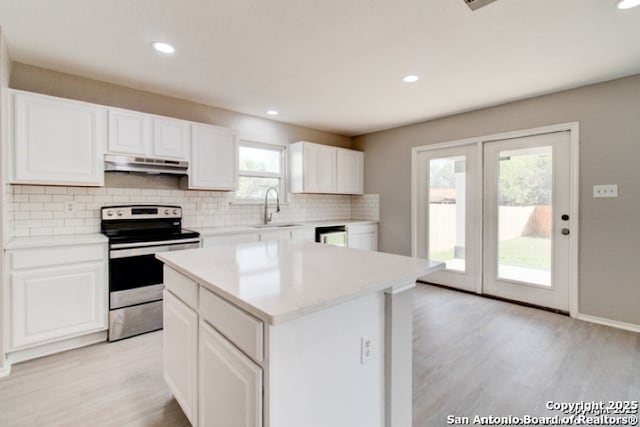 kitchen featuring tasteful backsplash, light wood-style floors, under cabinet range hood, a sink, and stainless steel electric stove
