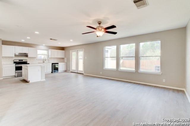 unfurnished living room with light wood-style floors, ceiling fan, visible vents, baseboards, and beverage cooler