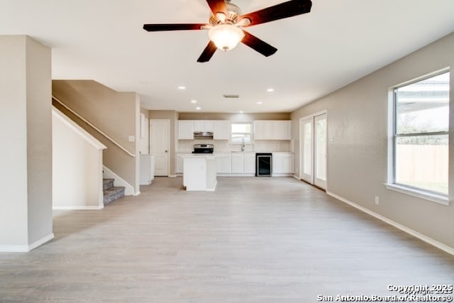 unfurnished living room featuring baseboards, a sink, light wood-style flooring, and wine cooler