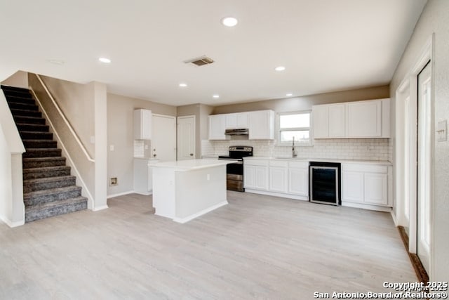 kitchen with beverage cooler, decorative backsplash, stainless steel range with electric cooktop, and a sink