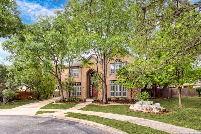 traditional home featuring brick siding, fence, and a front yard