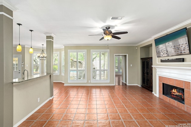 unfurnished living room with a tile fireplace, crown molding, visible vents, tile patterned flooring, and ceiling fan with notable chandelier