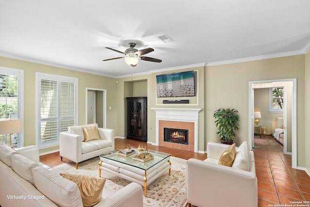 living area with a tile fireplace, plenty of natural light, ornamental molding, and a ceiling fan
