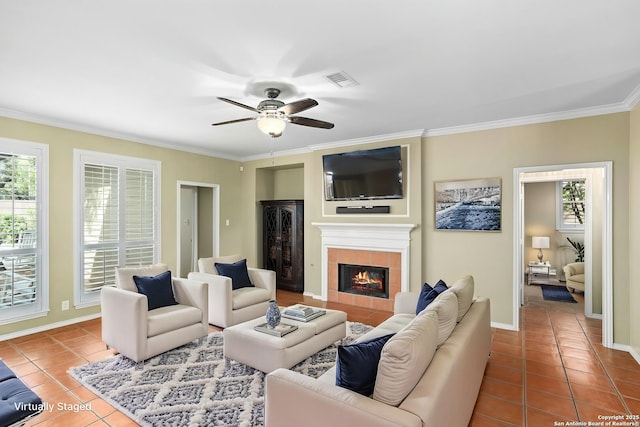 tiled living area with a ceiling fan, a healthy amount of sunlight, a fireplace, and crown molding